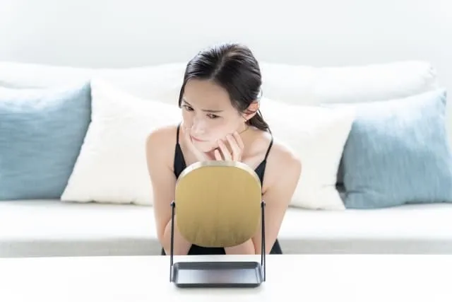 鏡で顔を見て肌トラブルに悩んでいる女性