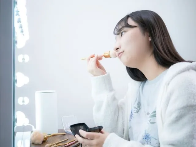 自宅で鏡を見ながらメイクしている女性